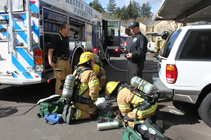 Three firefighters in uniform kneeling beside a fire engine, packing or taking inventory of equipment